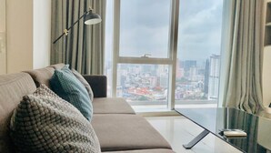 A modern living room with a sofa, a glass coffee table, and a view of a cityscape through large windows. - WELL-SHAPED Suites At PLATINUM KLCC (Kuala Lumpur)
