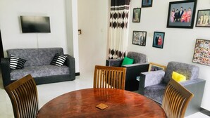 A living room with a round wooden table and four chairs, a grey sofa, and a television mounted on the wall. - Charming 1-bedroom house in beautiful Kandy with WiFi (Kandy)