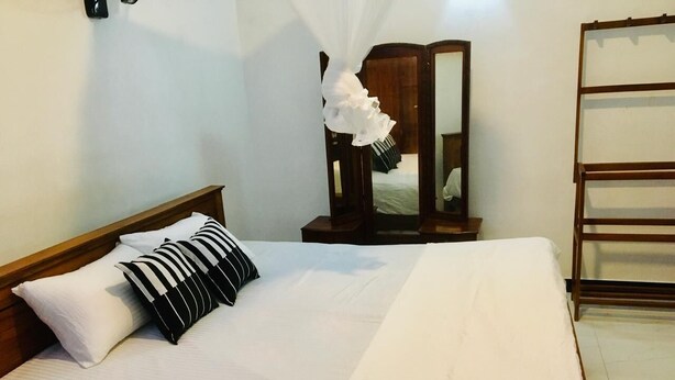 A neatly made bed with white bedding and striped pillows, a wooden nightstand with a mirror, and a wooden ladder against the wall. - Charming 1-bedroom house in beautiful Kandy with WiFi (Kandy)