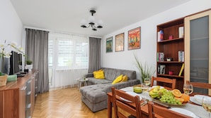 A modern living room with a grey sofa, wooden dining table, and a bookshelf. - Lumina 2-room apart near Złote Tarasy (Warsaw)