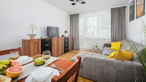 A modern living room with a grey sofa, wooden dining table, and a TV on a wooden cabinet. - Lumina 2-room apart near Złote Tarasy (Warsaw)