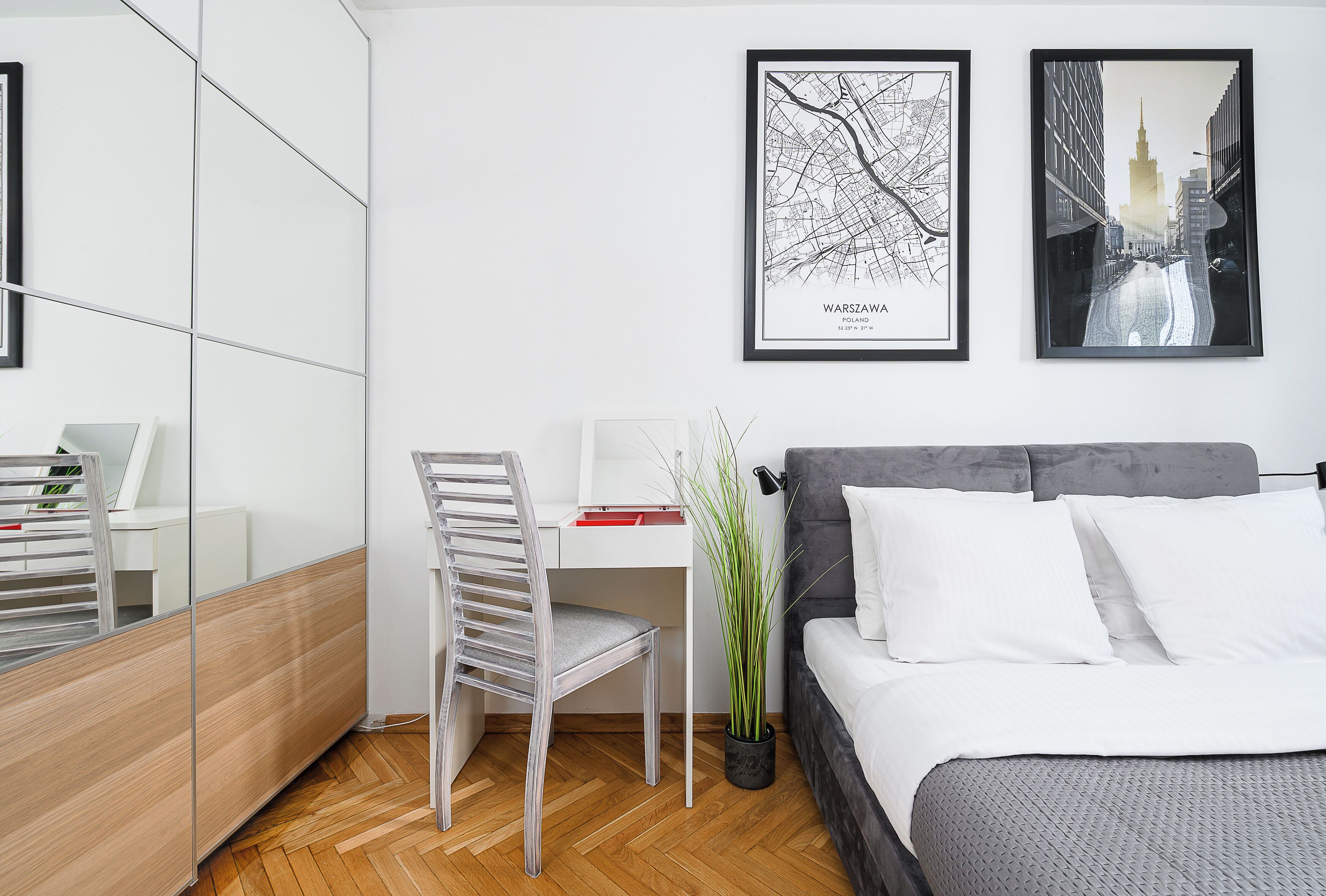 A modern bedroom with a bed, a desk, and a chair. There are framed pictures on the wall.