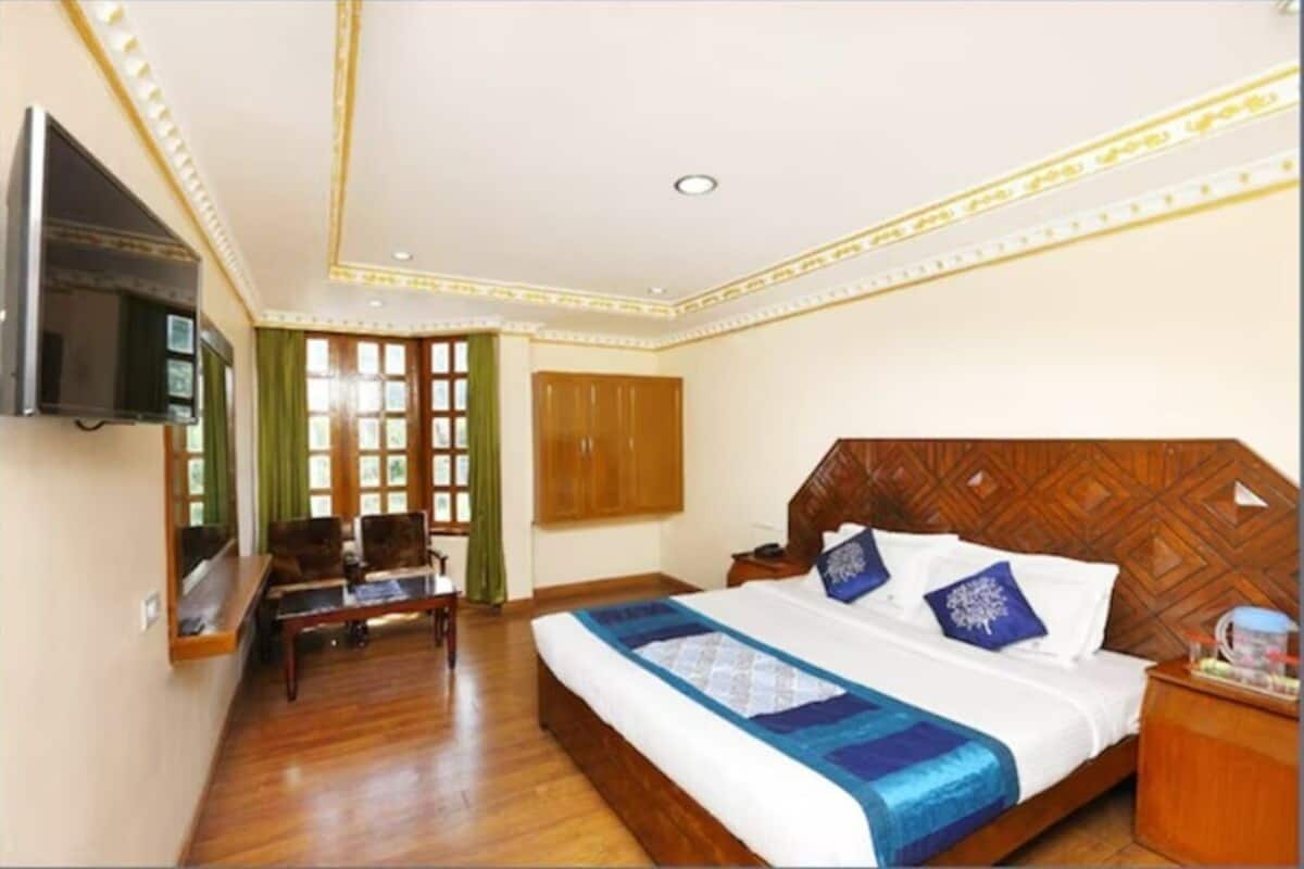 Una habitación de hotel con una cama de madera, un televisor instalado en la pared, un armario de madera y una cortina verde.