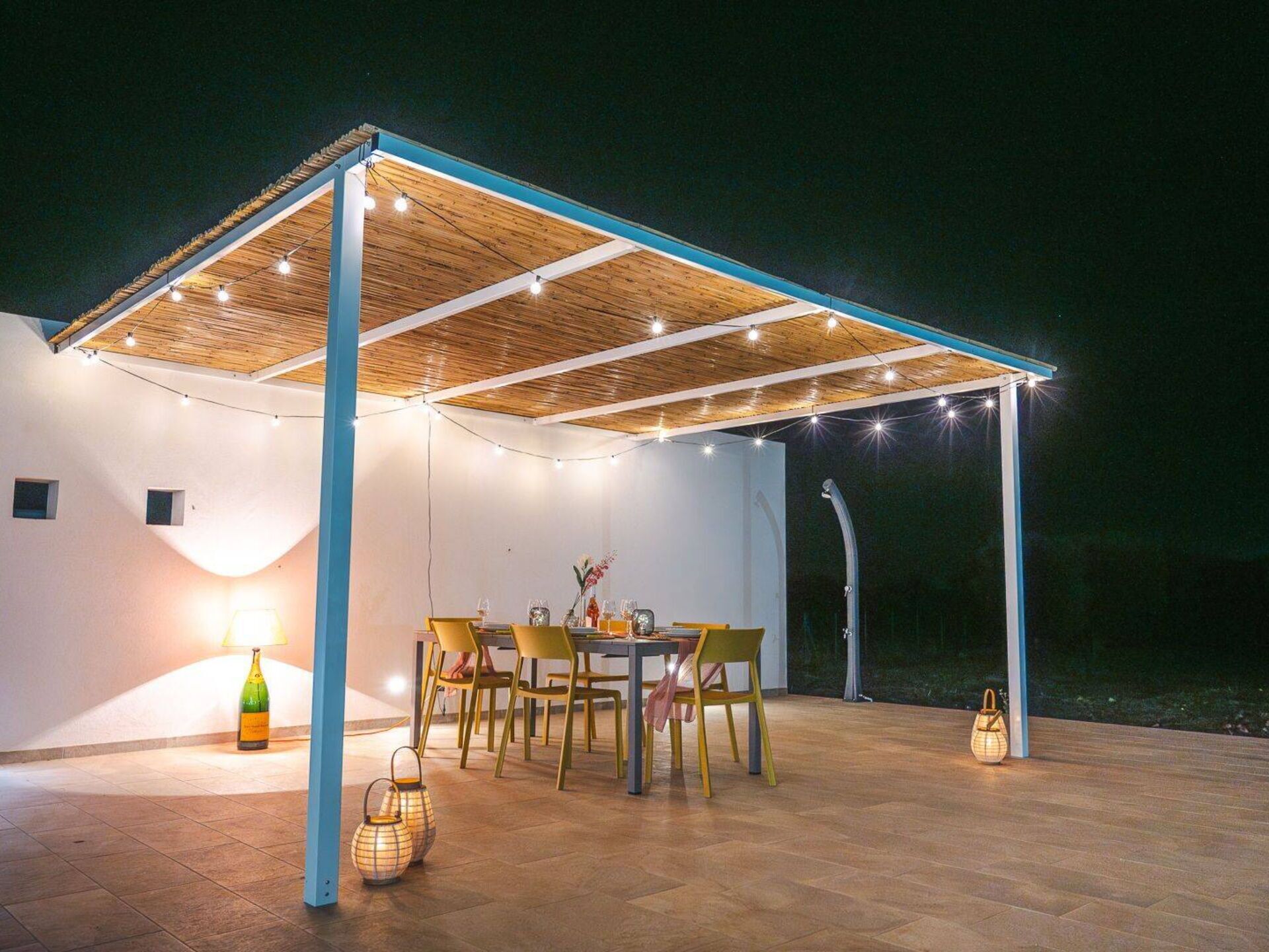 An outdoor patio area with a wooden pergola, string lights, and a table set for dining.