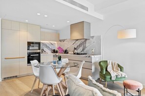 A modern kitchen with a dining area, featuring a marble backsplash, stainless steel appliances, and a minimalist design.