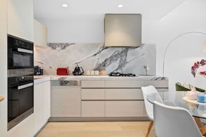 A modern kitchen with built-in appliances, a marble backsplash, and a glass dining table.