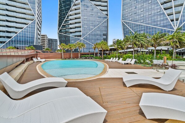 A rooftop pool area with lounge chairs and a view of modern buildings.