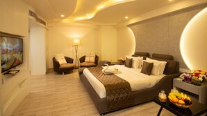 Een moderne hotelkamer met een groot bed, twee fauteuils, een flatscreen televisie en een nachtkastje met fruit.