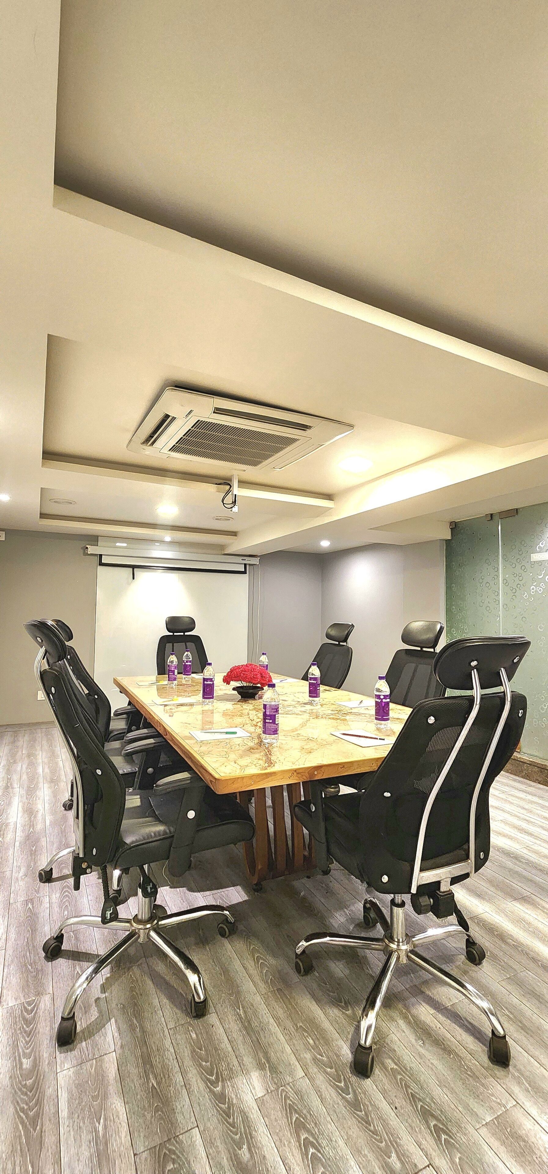 A conference room with a wooden table, black chairs, and a projector screen.