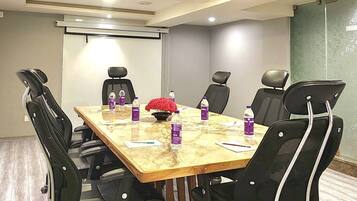 Un salón de conferencias con una mesa de madera, sillas negras y una pantalla de proyector.