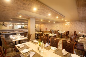 Un restaurante con techo y paredes de madera, varias mesas de comedor con sillas, y una zona de bar al fondo.