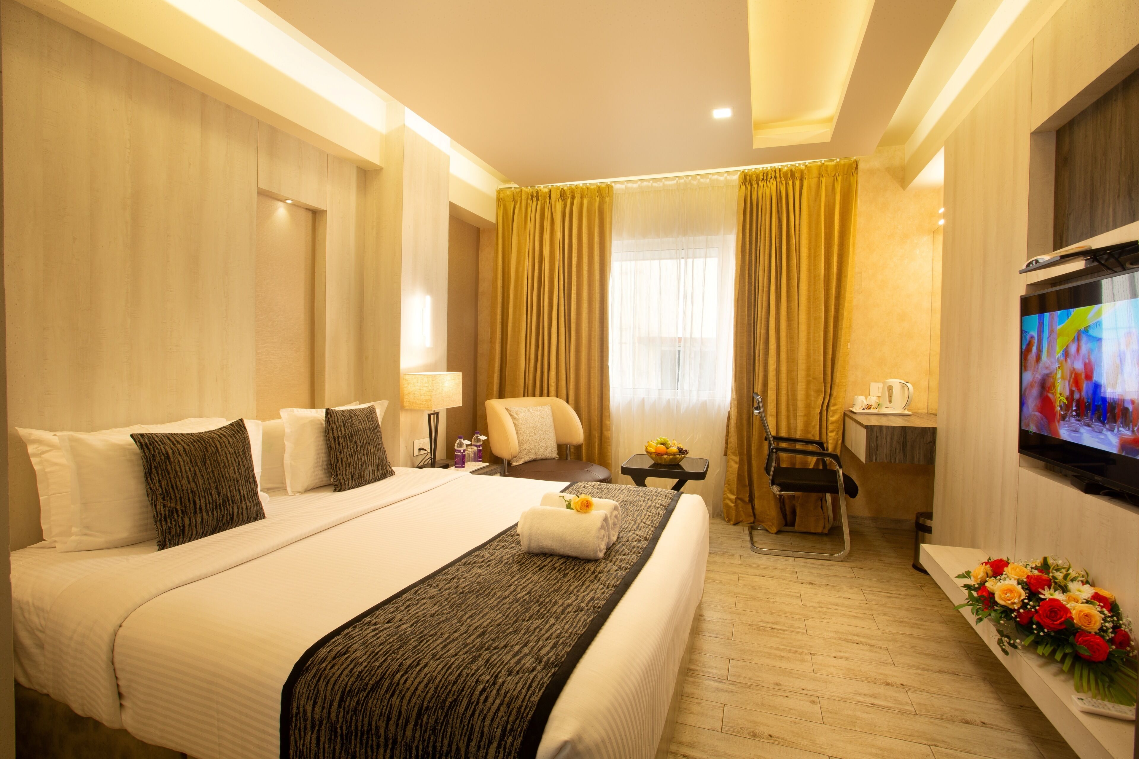 A hotel room with a large bed, a desk with a chair, a TV, and a bouquet of flowers.