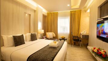 A hotel room with a large bed, a desk with a chair, a TV, and a bouquet of flowers.