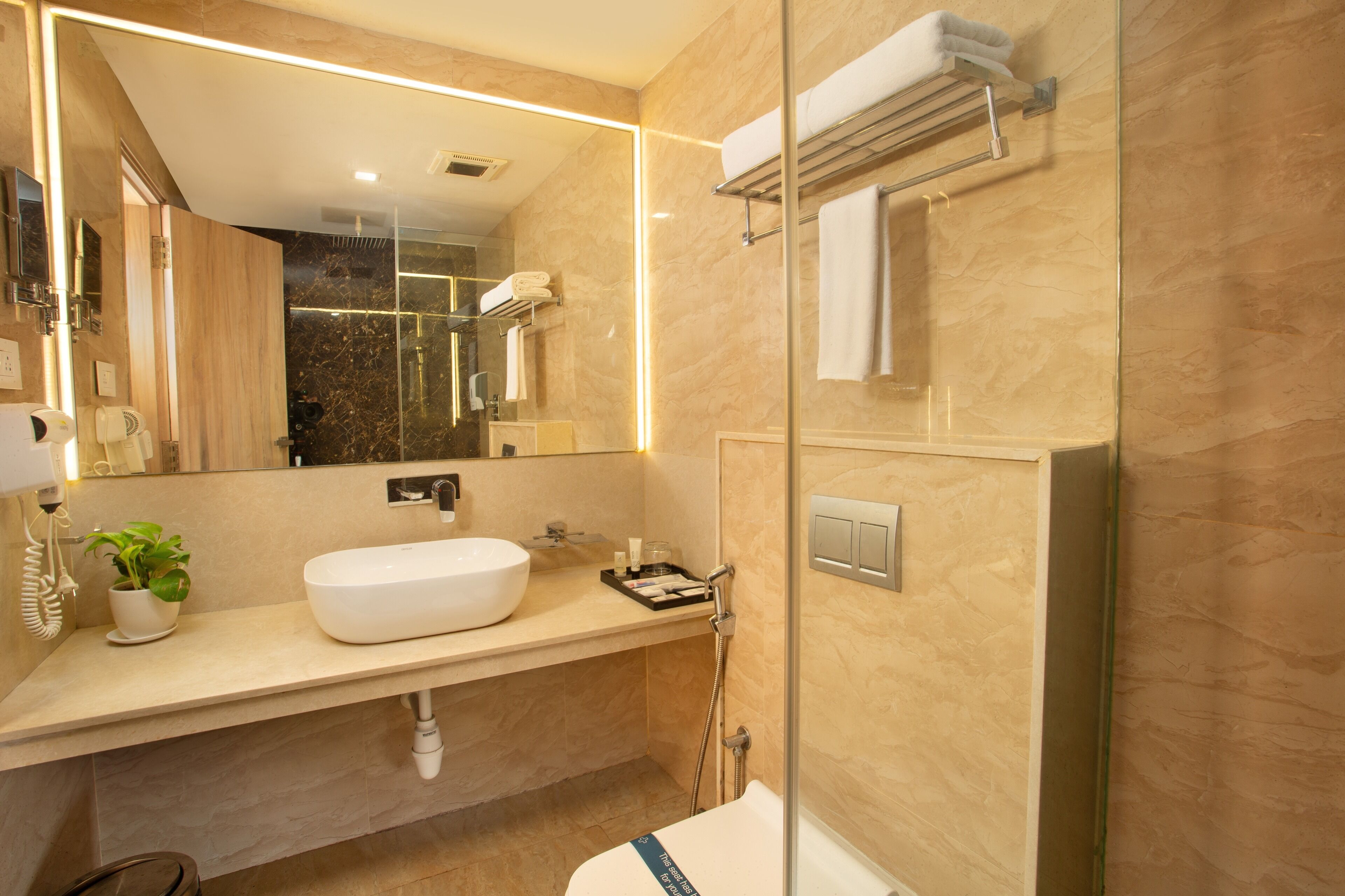 Une salle de bain moderne avec un grand miroir, un lavabo blanc, une douche en verre et un porte-serviettes.
