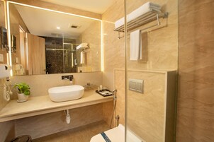 A modern bathroom with a large mirror, a white sink, a glass shower enclosure, and a towel rack.