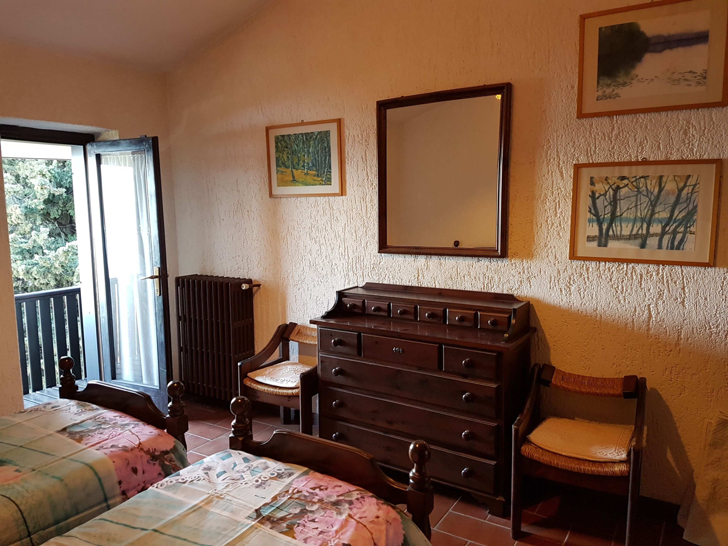 A bedroom with a bed, a dresser, a chair, and a balcony.