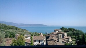 A coastal village with traditional architecture, a clear view of the sea, and a hilly landscape in the background. - Antico Fienile Belvedere (Gardone Riviera)