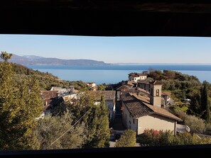 A coastal village with terracotta-roofed buildings, a clear view of the sea, and a hilly backdrop. - Antico Fienile Belvedere (Gardone Riviera)