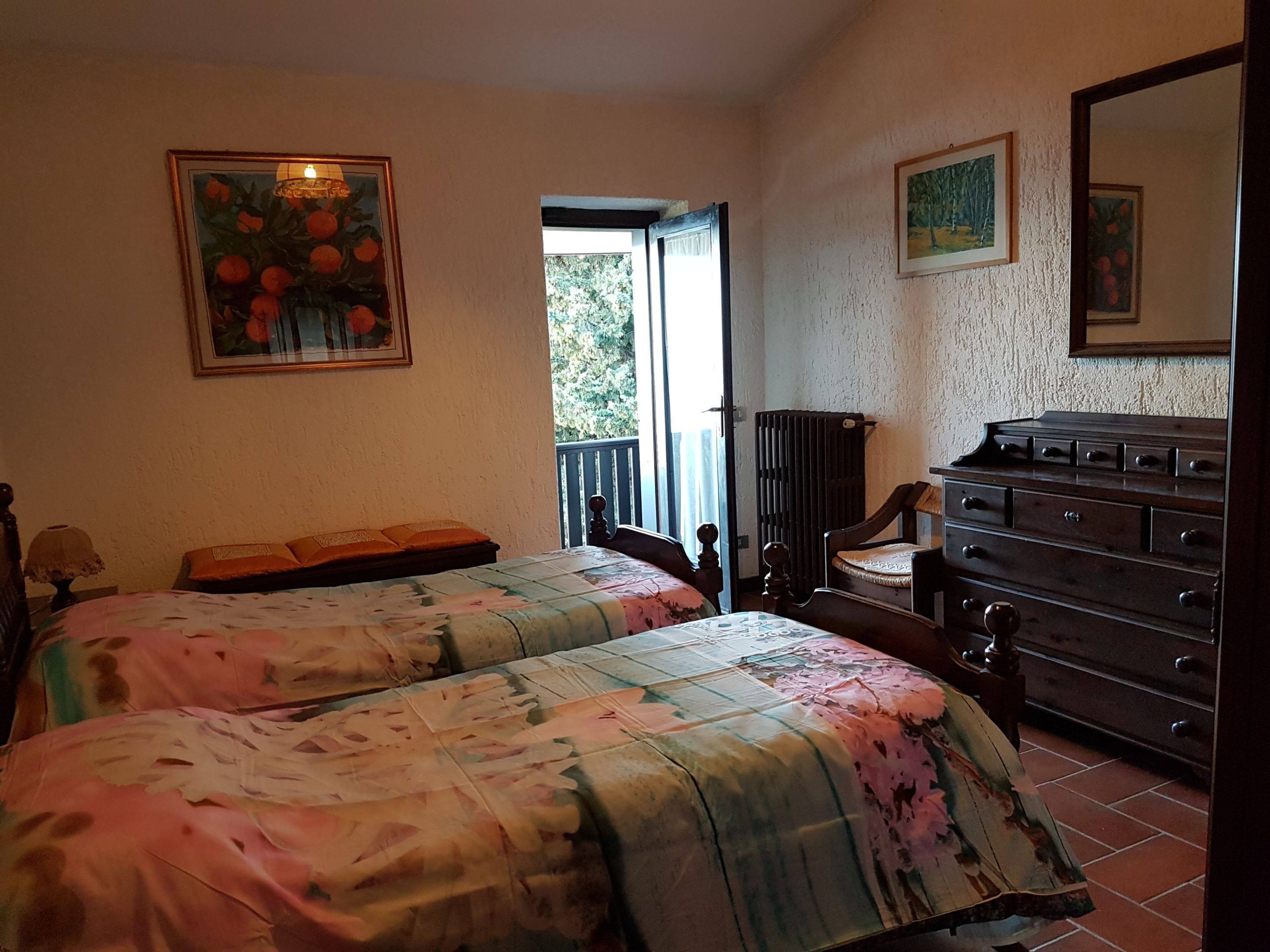 A bedroom with two beds, a dresser, and a chair. There is a window with a view of greenery outside.