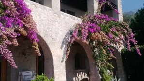 Un edificio con fachada de piedra, arcos en las entradas y un balcón. Hay plantas en macetas y un coche aparcado delante.
