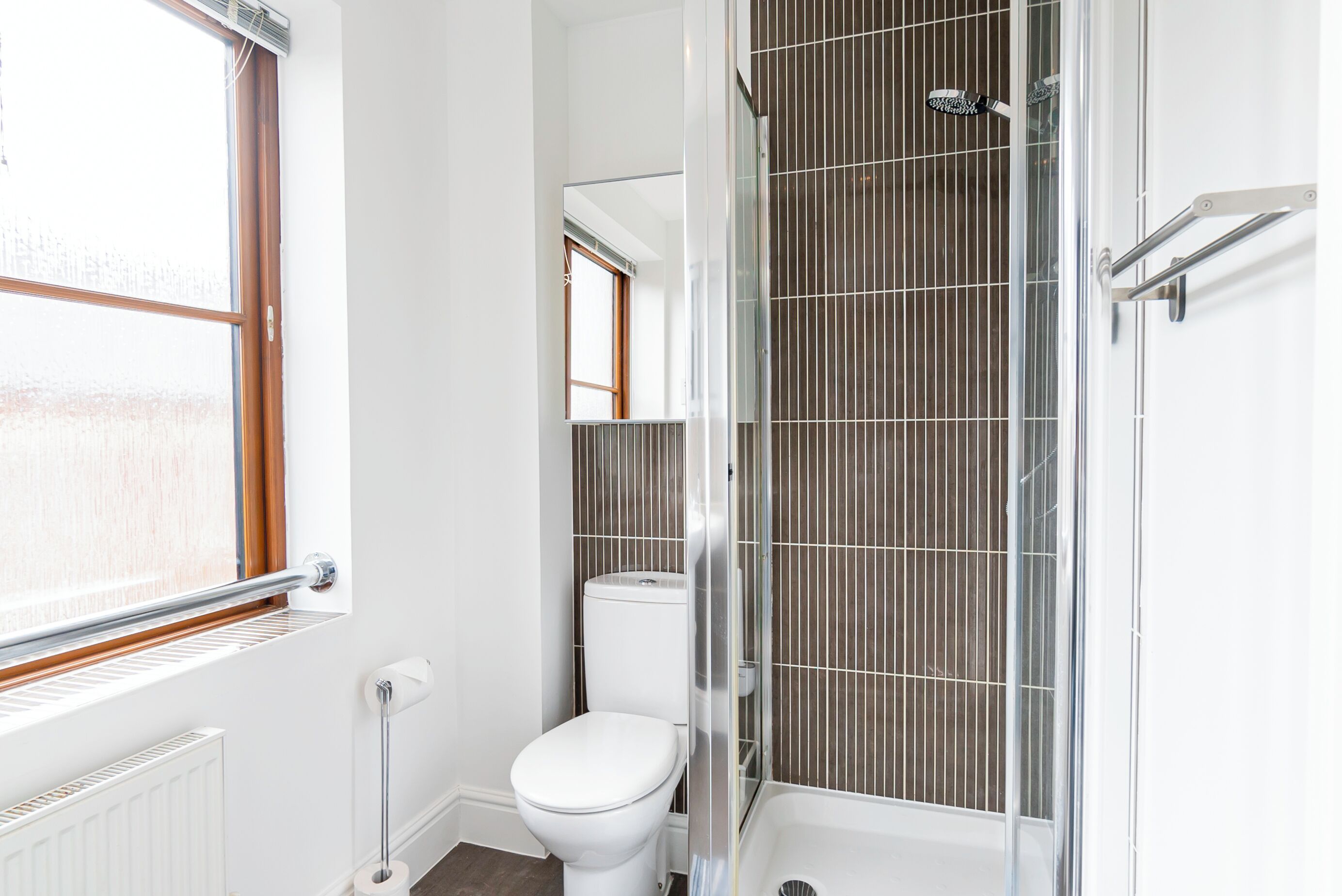 A modern bathroom with a toilet, shower, and a window.