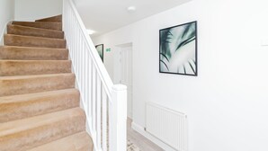 Una escalera con peldaños alfombrados en color beige y barandillas blancas, que conduce a una habitación con pared blanca y un cuadro abstracto enmarcado.