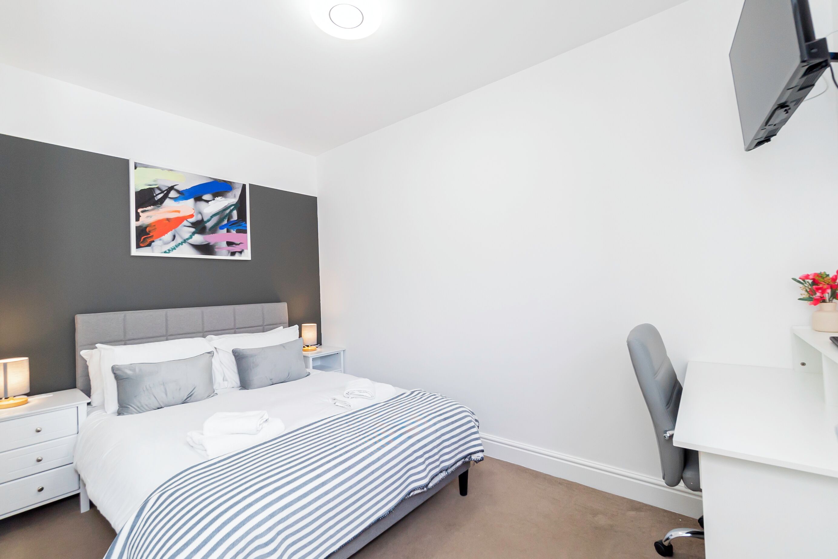 A modern bedroom with a bed, bedside tables, a desk, and a chair.