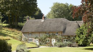 A thatched-roof house with a garden, a bench, and a picnic table.