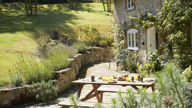 A rustic stone house with a thatched roof, a stone wall, and a garden with a picnic table set up outside.