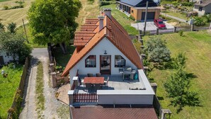 Una casa con techo inclinado, un patio con mobiliario exterior y vista a un paisaje verde.