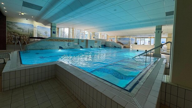Una piscina interior con varias pistas, paredes de azulejos e iluminación empotrada en el techo.