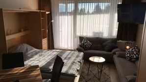 Una habitación de hotel compacta con cama, escritorio, sofá y televisor.