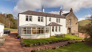 A two-story house with a conservatory, a stone chimney, and a grassy yard with a pathway.