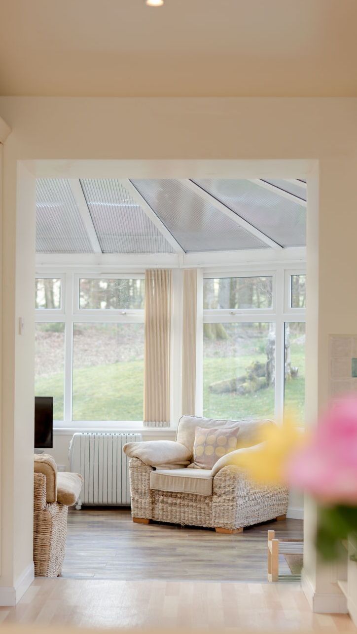 A cozy room with a wicker sofa, a television, and a view of a garden through large windows.