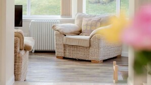 A cozy room with a wicker sofa, a television, and a view of a garden through large windows.