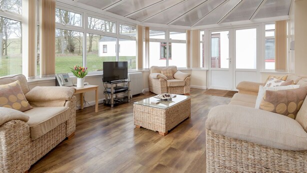 A spacious living room with wicker furniture, large windows, and a flat-screen TV.