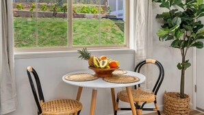 A dining area with a round table, two wicker chairs, a fruit bowl, and a potted plant. - Marbella Lane Nohea Stylish Home Makaha (Waianae)