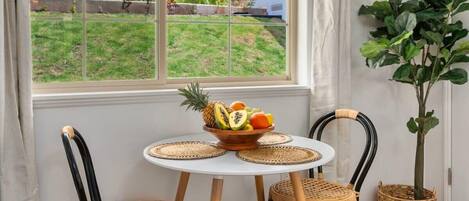 A dining area with a round table, two wicker chairs, a fruit bowl, and a potted plant.