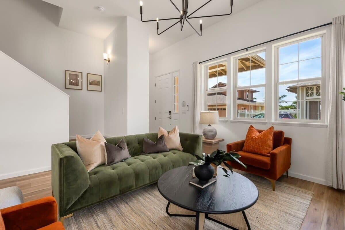 Een woonkamer met een groene bank, een ronde salontafel en een uitzicht op een huis door grote ramen.