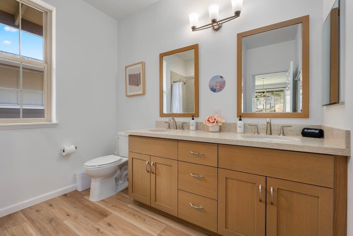 Une salle de bain avec des toilettes, des meubles en bois, un lavabo avec un miroir et une fenêtre.