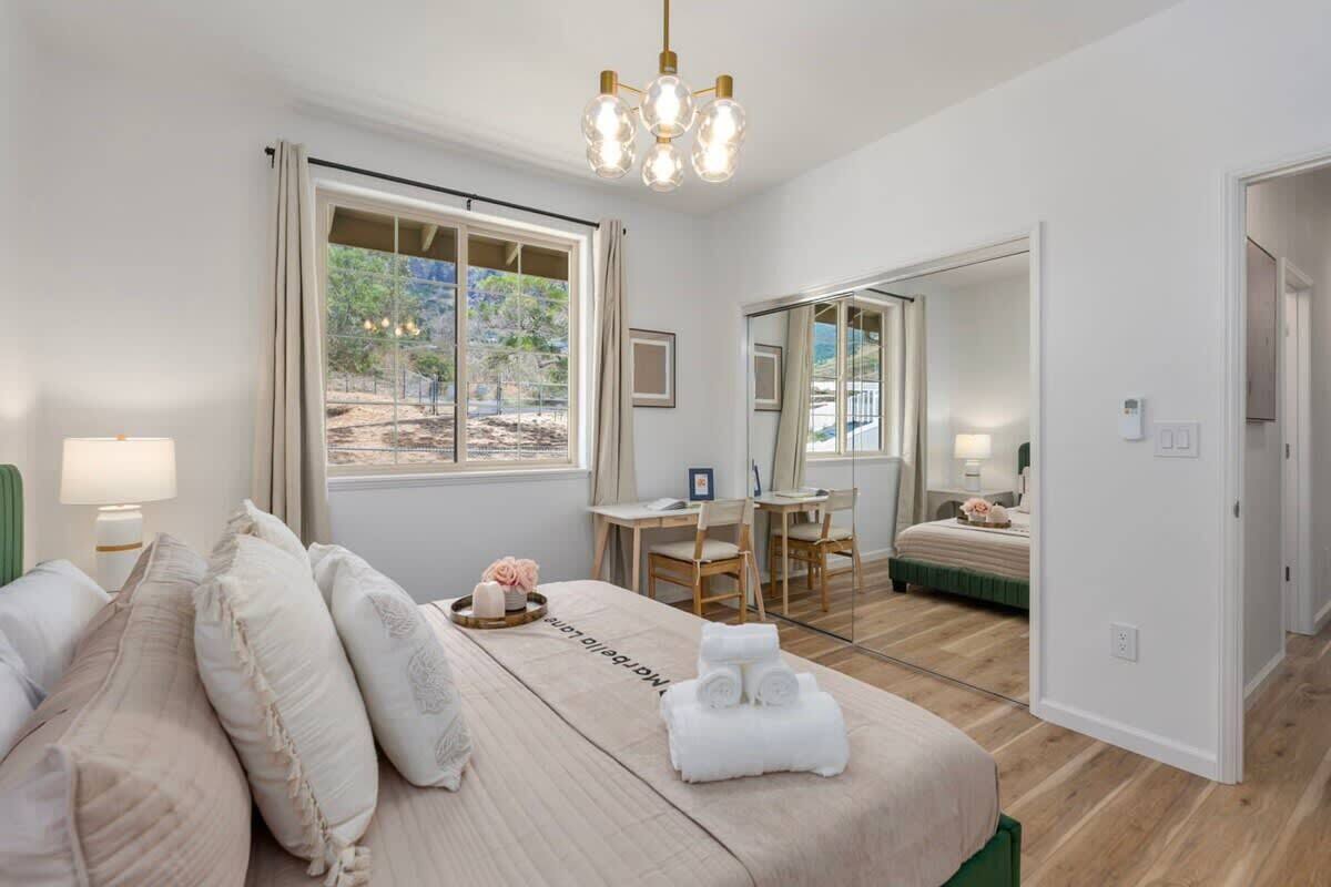 A bedroom with a bed, bedside table, lamp, and a view of the outdoors through a window.