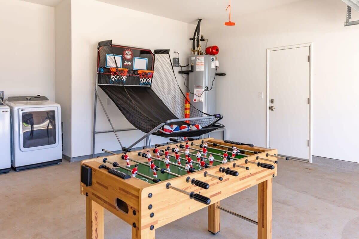 A foosball table in a room with a small basketball hoop and a water heater.