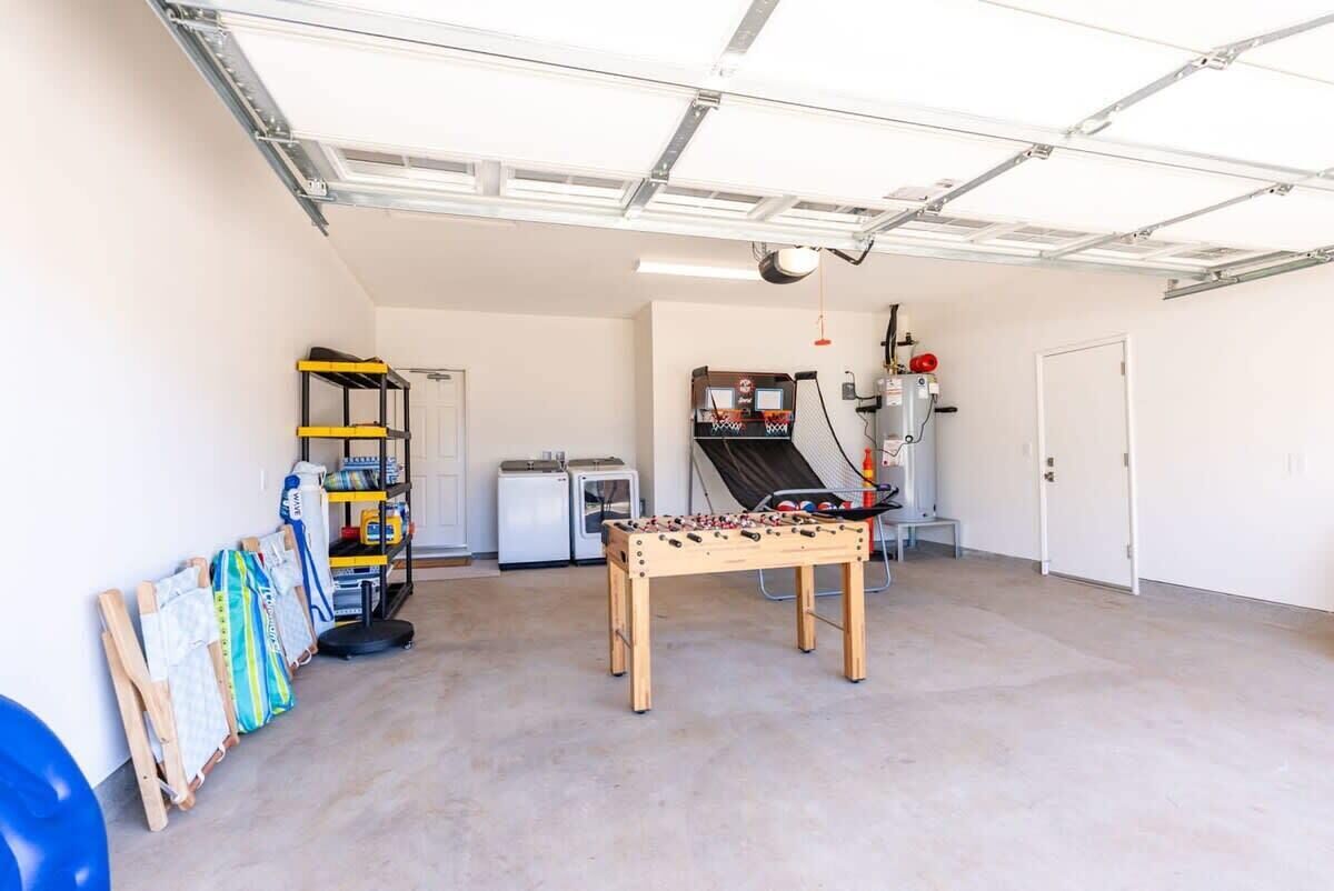 Un garaje con mesa de fútbol, un estante con productos de limpieza y un refrigerador pequeño.