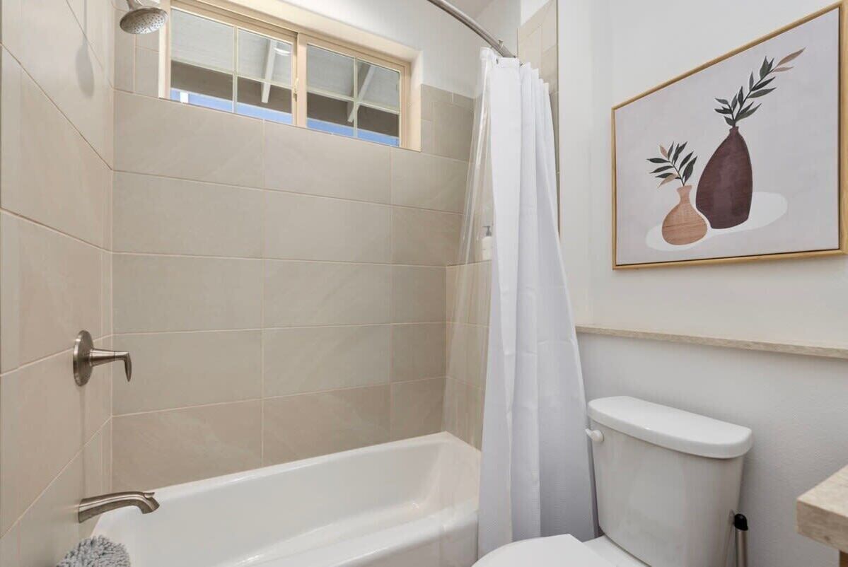 Une salle de bain avec une baignoire, des toilettes, un rideau de douche et un tableau encadré au mur.