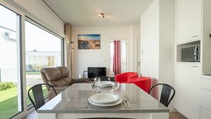 Un espace repas moderne avec une table en verre, deux chaises rouges et un fauteuil en cuir marron.