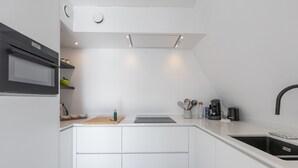 Una cocina moderna con armarios blancos, horno empotrado, microondas, pileta y una encimera con diversos electrodomésticos y utensilios.