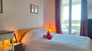 Een hotelkamer met een bed, nachtkastje, lamp, raam met gordijnen en uitzicht.