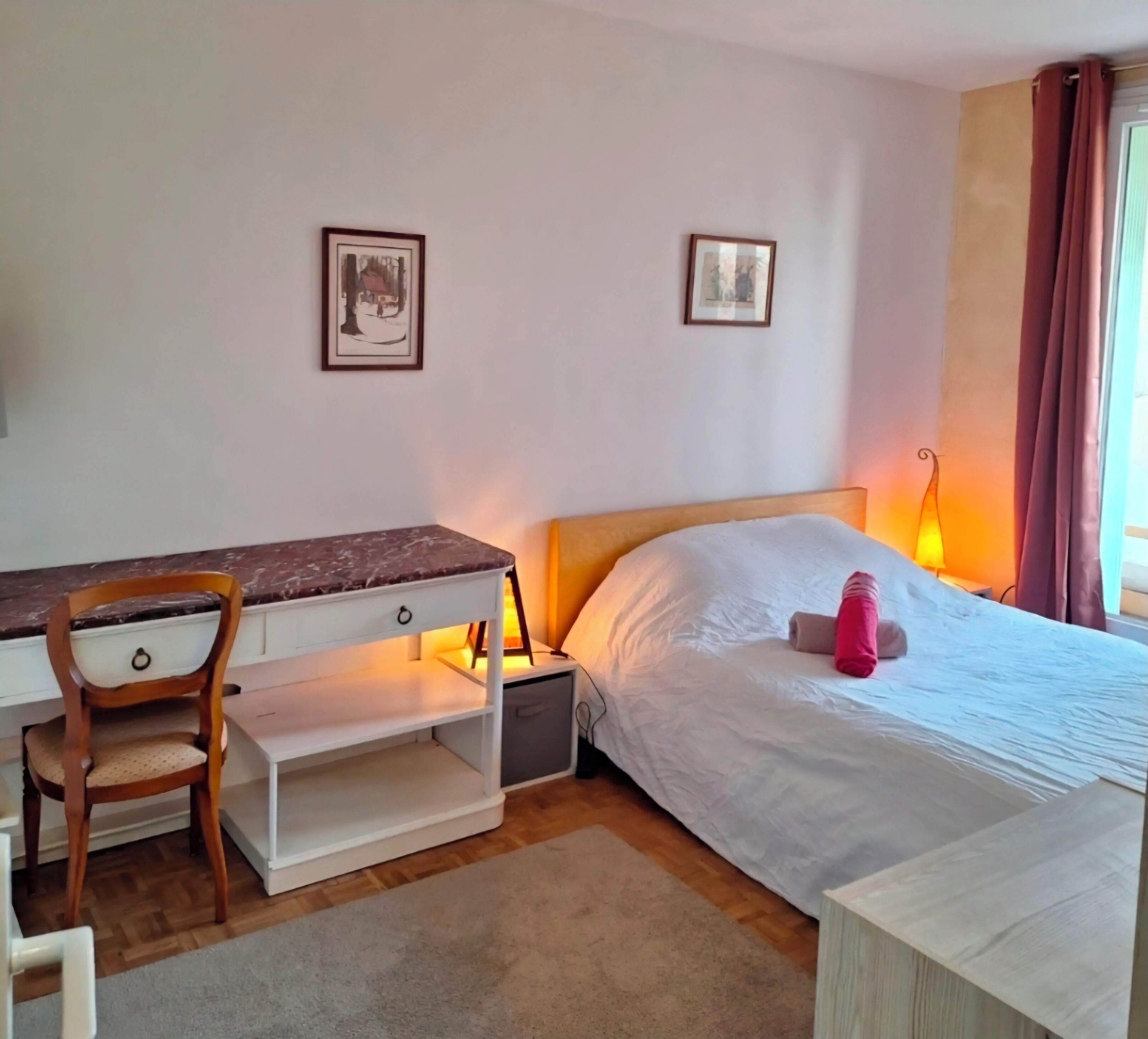 Un dormitorio con cama, escritorio, silla y dos cuadros en la pared.