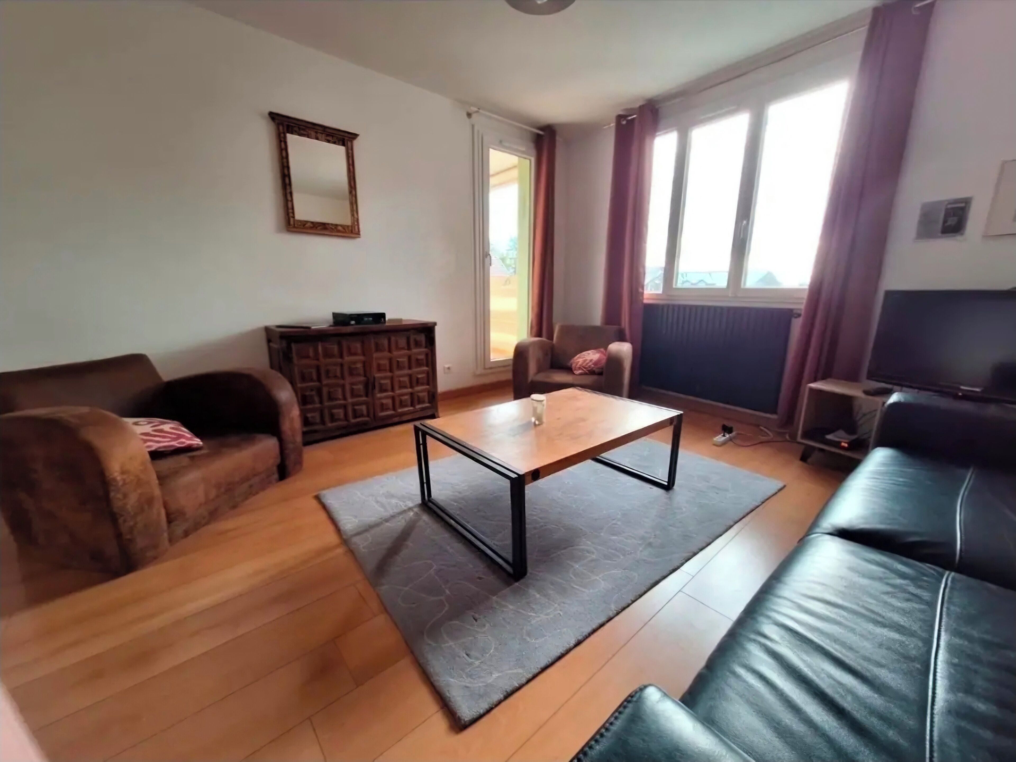 Ein Wohnzimmer mit braunem Ledersofa, einem Holztisch, einem braunen Schrank, einer schwarzen Lederliege und einem Fernseher auf einem Lowboard.