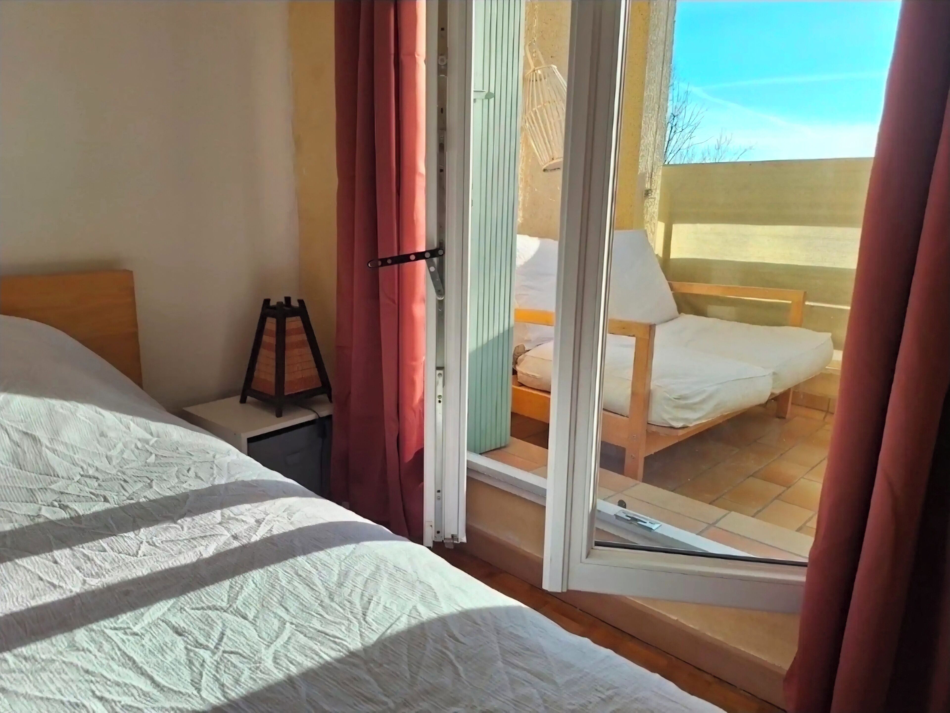 Quarto com duas camas, uma mesinha e janela com cortinas.